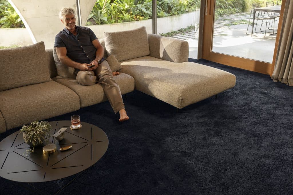 Dark blue carpeted lounge with man relaxing on a couch.