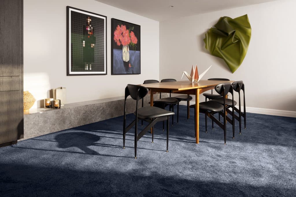A dining table setup in a navy carpeted room, decorated with art.
