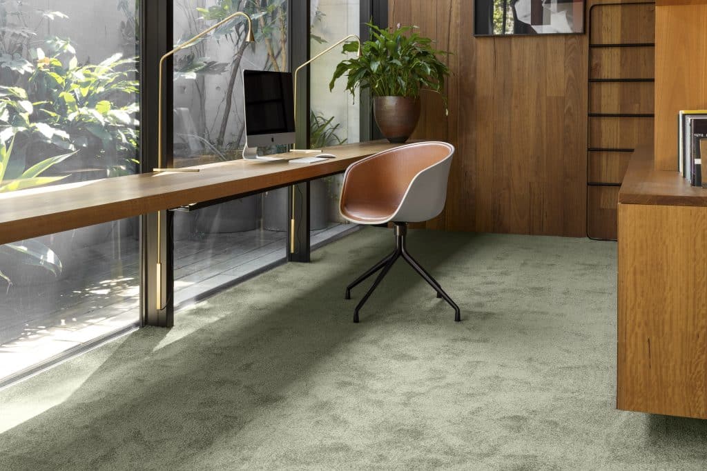 A green carpeted study room with a chair, overlooking a small garden area.